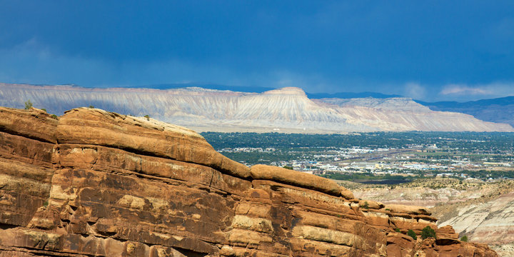 Afternoon light on the steep, sloping bluffs of the eastern side of Colorado National Monument, with the town of Grand Junction and distant mountains, as seen from Rim Rock Drive