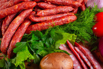 Hunting smoked sausages isolated on white background. Sausage with greens and vegetables on a wooden round board