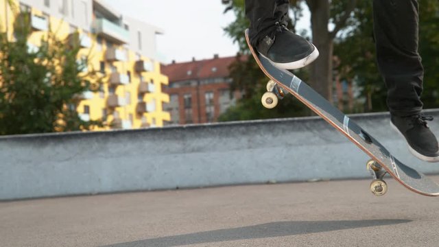 SLOW MOTION CLOSE UP: Unrecognizable young skateboarder dude lands a perfect kickflip in the concrete park. Cool skater having fun in the city does a flip trick on a sunny day. Cinematic skateboarding
