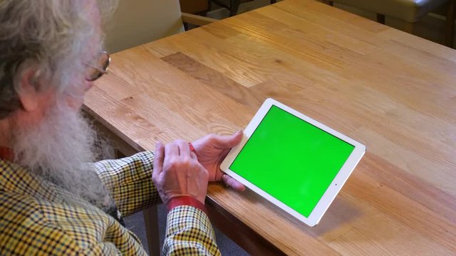 Older man with beard watching tablet device and swiping left