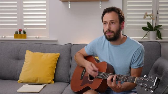 An authentic STATIC SHOT of an average man playing his acoustic guitar and singing with passion, in a minimalistic lounge.