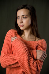 A beautiful young brunette girl in an orange knitted sweater poses against a dark background.