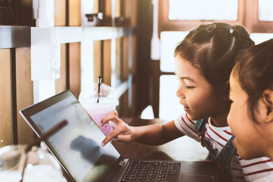 Two cute asian child girls using and playing on laptop in the cafe together with fun and happiness - Powered by Adobe