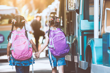 Asian pupil kids with backpack holding hand and going to school with school bus together. Back to school concept.