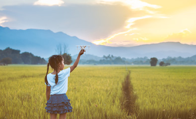 Cute asian child girl playing with toy wooden airplane in the field at sunset time in vintage color tone