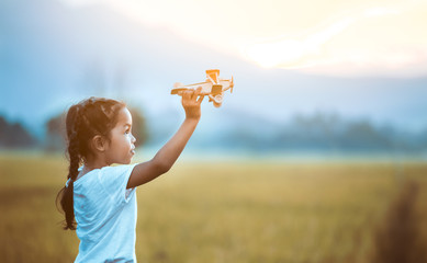 Cute asian child girl playing with toy wooden airplane in the field at sunset time in vintage color tone © pingpao