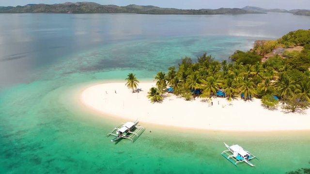 Aerial rising drone shot away from a beautiful, white sand isle, palm trees and Paraw boats, at Pass island, in Philippines