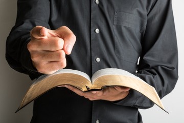 Closeup on a Priest Holding a Bible and Pointing Finger