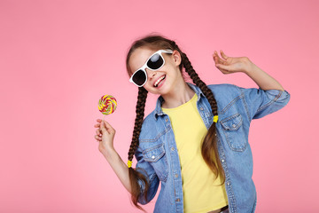 Young girl with lollipop and sunglasses on pink background
