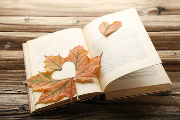 Dry maple leaf with heart and open book on brown wooden table
