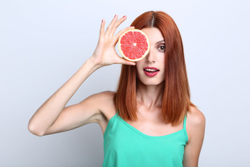 Beautiful redhaired woman with grapefruit on grey background