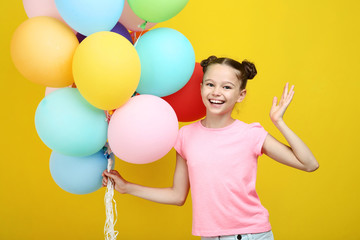 Fototapeta na wymiar Beautiful young girl with colored balloons on yellow background