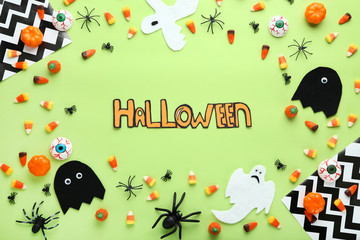 Inscription Halloween with candies and paper decorations on green background