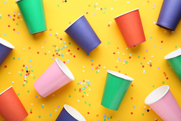 Colorful paper cups with confetti on yellow background