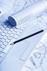 Blueprints with a drafting pencil and laptop on top of them