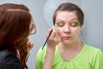 Professional visage artist applying artistic make-up on woman's face in salon.