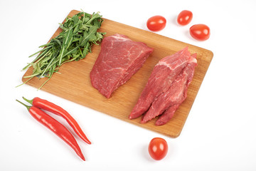 Sliced raw beef on cutting board and vegetables isolated on white background