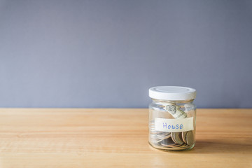 money coin in a glass jar on wooden desk, Saving money for buy house concept