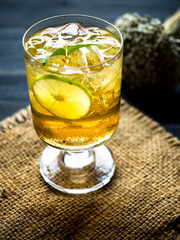 Glass of lemon tea with ice on black wood floor with dry flower