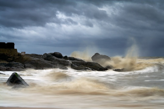 Stormy Evening with large wave curls and spills over itself as it crashes against the rocks in Bekal Beach, Kasargod, Kerala, India.