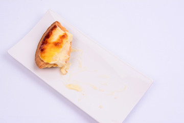 Half eaten cheese tart pastry in a white ceramic plate isolated on white background.