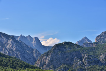peaks of the Taurus mountains covered with green vegetation, against the blue sky and clouds