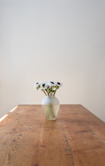 Rustic wooden table with vase of white anemone flowers against neutral wall (selective focus)
