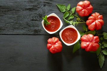 tomato ketchup.Tomato sauce.The recipe for ketchup. home made sauce ketchup in two white plates, large ripe red tomatoes with leaves, basil, marjoram on a black wooden background with copy space.