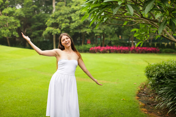 portrait of carefree young woman in white dress posing in green summer park