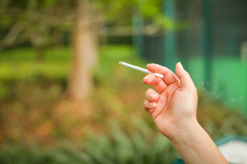 Female hand with smoking cigarette on blurred green park background