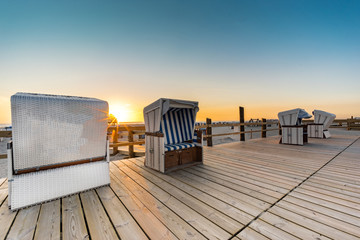 Strandurlaub an der Nordsee, Strandkorbe auf einer Holzterasse - Sonnenuntergang im Hintergrund - obrazy, fototapety, plakaty