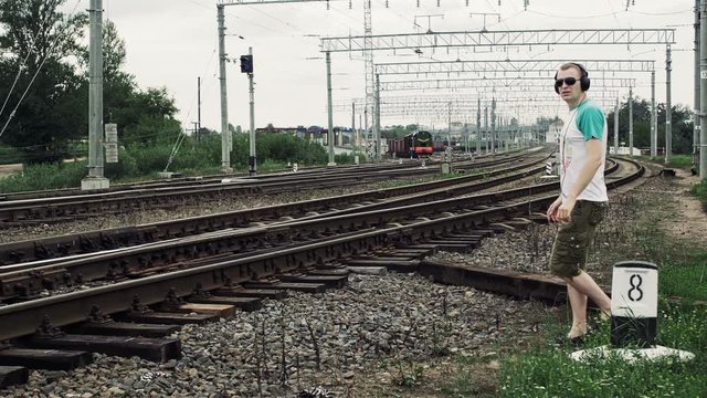 Guy with headphones crosses a railway or railroad in the wrong place, life threatening
