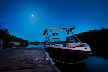 A wakeboard boat docked on Lake Joseph in the evening with the moon in the background.