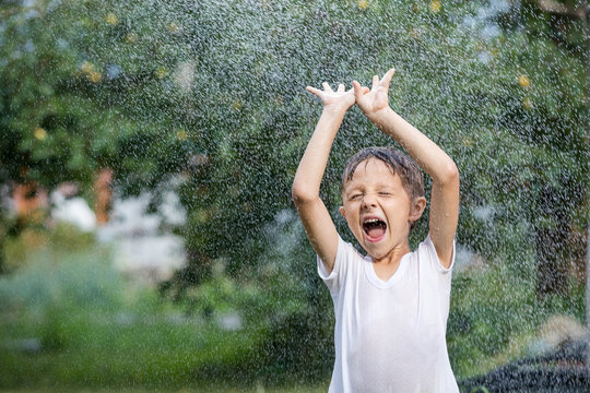 Happy little boy pouring water from a hose.