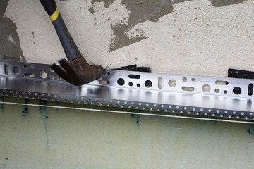 Hammer on metal profile for installing insulation on white exterior wall of house. DIY and home improvement concept.