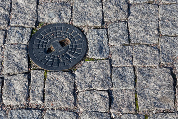 A manhole cover on a pavement of granite blocks