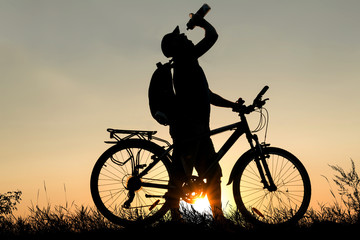 Fototapeta na wymiar Silhouette of a man drinking water with bicycle at sunset