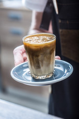 Barista in coffee shop holding cup with ice coffee.
