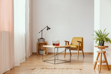 Plant on wooden stool in white apartment interior with yellow armchair at table and lamp. Real photo