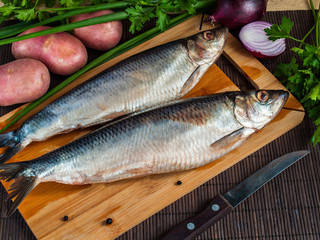 On the wooden cutting board are two salted fish herrings