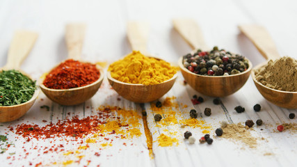 Row of wooden spoons filled with various multicolored spices and composed on wooden table