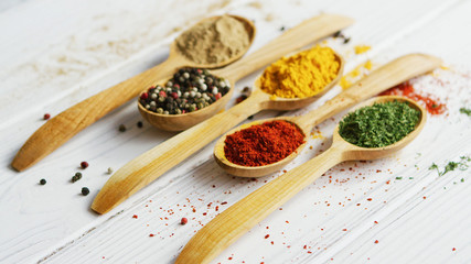 Arrangement of small wooden spoons with assortment of ground spices on wooden table