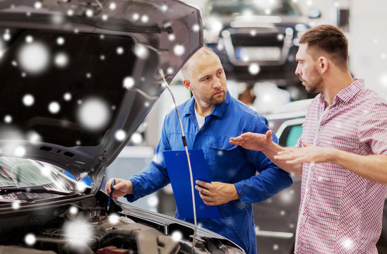 auto service, repair, maintenance and people concept - mechanic with clipboard and man or owner talking at car shop over snow