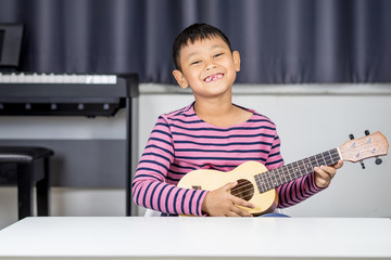 Asian boy  aged 7-8 Play ukulele in the room,  passionate love in music,  Child Development Concept