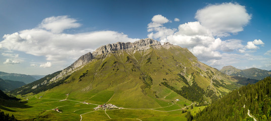 The Col des Aravis in the French Alps on a sunny day with clouds in the background. The green grass is standing out at the bottom of the mountain