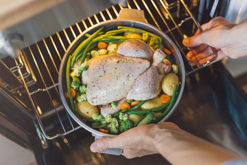 Cook putting raw chicken to the oven
