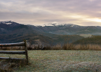 wooden fence on meadow with frozen grass. mysterious late autumn scenery with snow on tops of...
