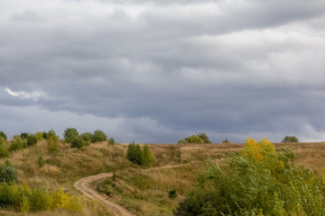 Fototapeta na wymiar A rural dirt road in the hill among the autumn landscape and large clouds.