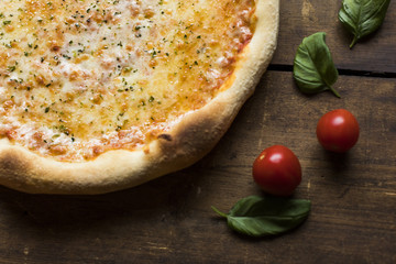 A part of a margherita pizza with a basil leaves and tomatoes on a vintage wood surface