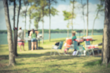 Motion blurred friend and family members enjoy barbecue on lakeside area. Portable picnic grills...